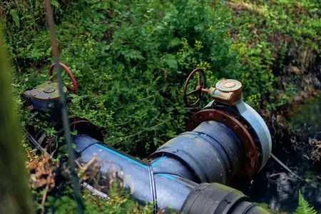 Наружная водопроводная труба с вентилем, на корродированном металлическом фланце видны ржавчина и мох