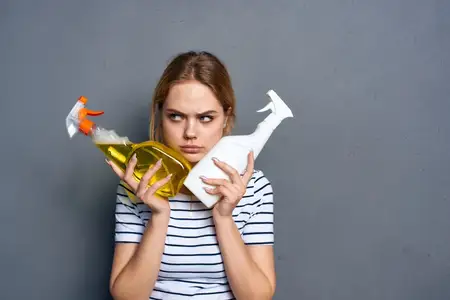 Уборщица держит в руках моющее средство, обрезанный вид, серый фон