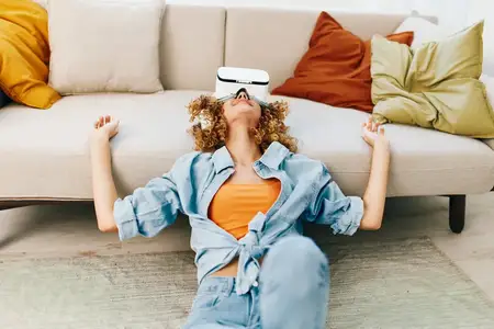 Улыбающаяся женщина наслаждается игрой в виртуальной реальности дома в VR-очках на диване