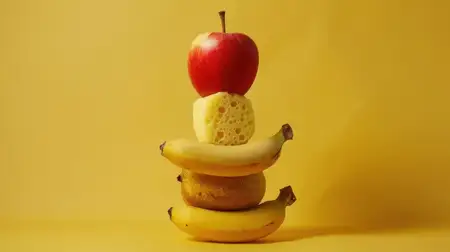 Творческая композиция из фруктов, включающая красное яблоко, бананы и губку на ярком желтом фоне