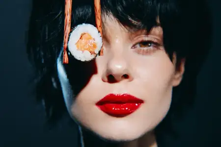 Модная женщина с красными губами игриво держит суши палочками