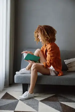 Молодая женщина с вьющимися волосами наслаждается чтением книги в стильной гостиной