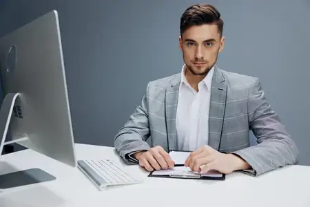 Менеджер в сером костюме сидит перед компьютером на сером фоне