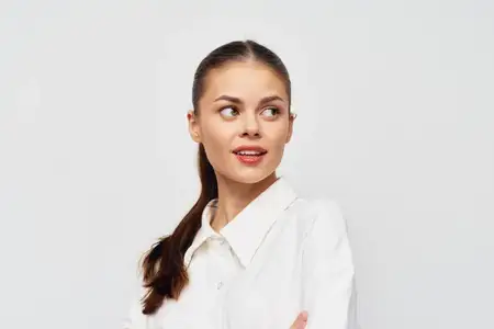 Молодая женщина с длинными каштановыми волосами, собранными в хвост, задумчиво смотрит в сторону