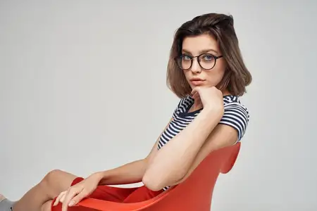 Красивая женщина в полосатой футболке сидит на красном стуле, у неё современная причёска