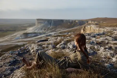 Женщина сидит на краю обрыва, любуясь захватывающим видом на долину и горы в спокойном путешествии-побеге от повседневности