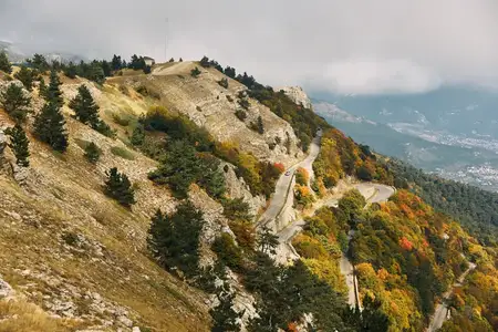 Живописная извилистая дорога, пролегающая через горы среди деревьев, облаков и природных пейзажей