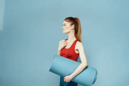 Спортивная женщина в красной футболке занимается на фитнес-коврике, демонстрируя стройную фигуру