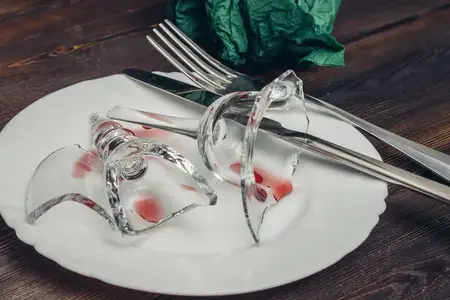 Разбитое стекло на тарелке, сервировка стола со столовыми приборами, деревянный стол