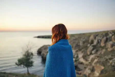 Женщина на природе, укрывшись одеялом, утром любуется пейзажем