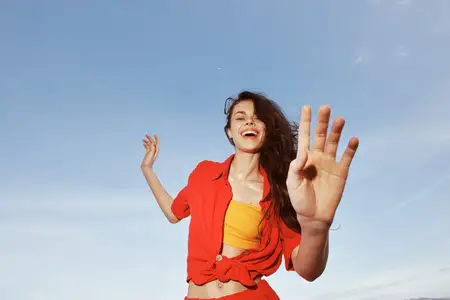 Радостное лето: улыбающаяся женщина в красной одежде танцует на пляже во время отпуска