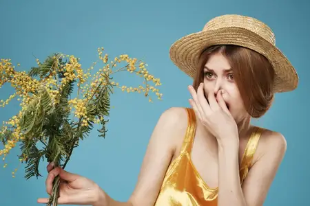 Весёлая женщина с букетом цветов в шляпе, украшенной мимозой, на голубом фоне