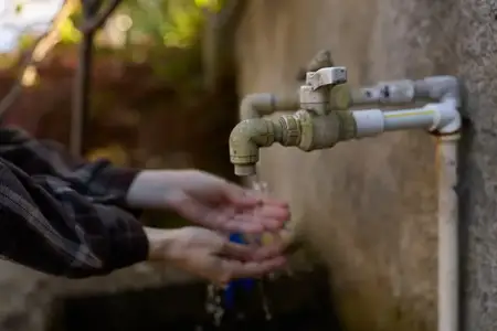 Руки под металлическим краном с текущей водой на улице