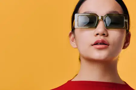 Модная молодая женщина в солнцезащитных очках и красной одежде позирует на желтом фоне