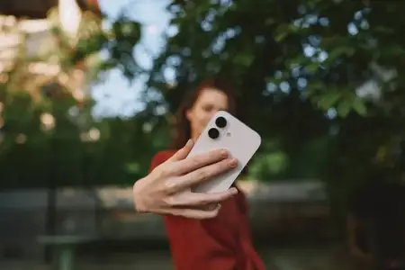 Повседневный уличный портрет женщины со смартфоном, делающей селфи при ярком естественном свете, расслабленное настроение, повседневная связь и самовыражение