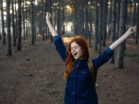 Счастливая женщина-туристка жестикулирует руками на природе в сосновом лесу, выражая радостные эмоции
