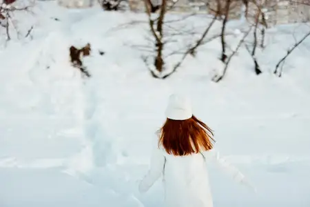 Молодая женщина улыбается, прогуливаясь в белом пальто, наслаждаясь зимним настроением и свежим воздухом