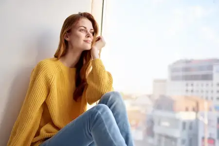 Красивая женщина лежит у окна с мечтательным взглядом