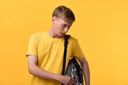 Юноша в желтой футболке с камуфляжным рюкзаком на ярком желтом фоне
