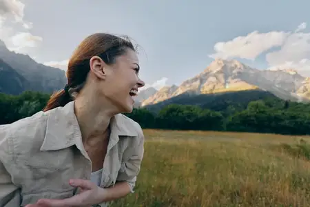 Яркая лайфстайл-сцена: женщина наслаждается природой, смех и движение, расслабленная поза, свежий воздух, живописный фон, тепло на открытом воздухе, красочный пейзаж