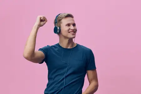 Веселый молодой мужчина в наушниках улыбается, слушая музыку на фоне ярко-розового фона
