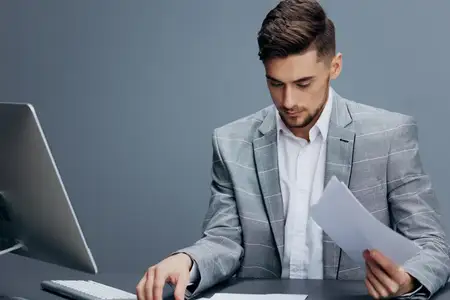 На столе лежат документы, рядом работает компьютер, за которым сидят бизнесмены