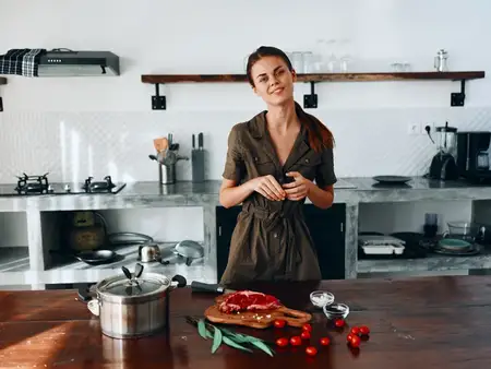 Женщина улыбается на кухне, готовит еду, используя мясо и овощи