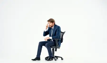 Бородатый мужчина в костюме сидит в офисном кресле, работает официально