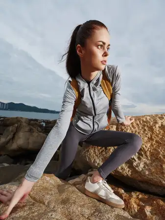 Спортивная молодая женщина в серой спортивной одежде позирует на каменистой местности, отражая силу и решительность на фоне спокойного открытого пространства, что идеально подходит для фитнес-тем