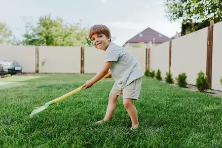Радостный мальчик занимается садоводством, используя грабли, чтобы помочь во дворе