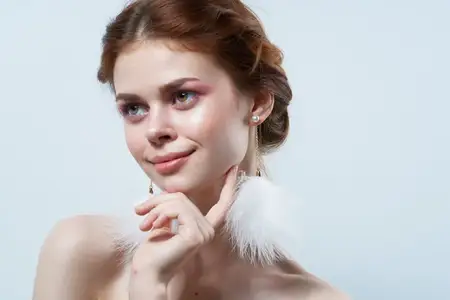 Жизнерадостная женщина с обнаженными плечами, пушистыми серьгами, косметикой и украшениями