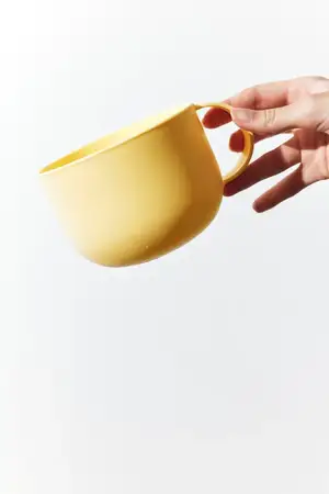 Рука держит жёлтую кружку со словом «cup» на белом фоне