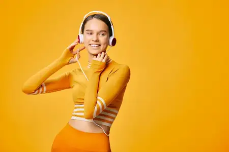 Атлетичная женщина в спортивном оранжевом костюме с музыкальными наушниками, готовая поза во время тренировки, подчеркивающая фитнес, движение и яркий цвет в динамичной студийной сцене