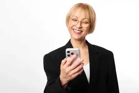 Пожилая женщина в очках улыбается, глядя на экран смартфона