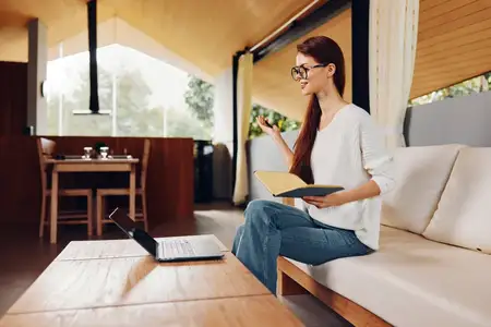 Улыбающаяся женщина работает за ноутбуком на диване в домашнем офисе