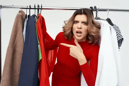 Симпатичная женщина в очках стоит рядом с одеждой, излучая моду, веселье и лёгкость на светлом фоне
