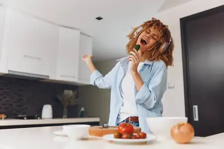 Счастливая женщина напевает на кухне, нарезая свежие помидоры ножом