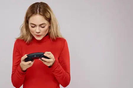 Женщина с геймпадом в руках, играет в игры, эмоции, образ жизни, досуг, красная рубашка, светлый фон