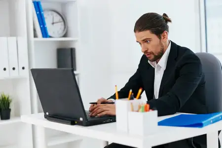 Менеджер работает за ноутбуком, на его лице отражаются эмоции, он похож на начальника