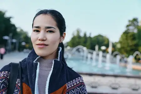 Сцена на открытом воздухе: женщина в стильной куртке в парке у воды и фонтана
