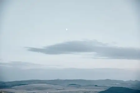 Величественный восход луны над далекими горами с клубящимися облаками в сумеречном небе