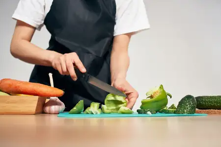 Повар в черном фартуке нарезает овощи на кухне крупным планом, процесс приготовления
