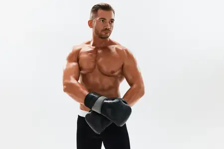 Спортсмен-бодибилдер в боксерских перчатках позирует в полный рост на фоне, обнаженный торс, пресс