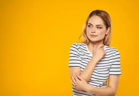 Женщина прикасается к себе руками на желтом фоне, улыбается