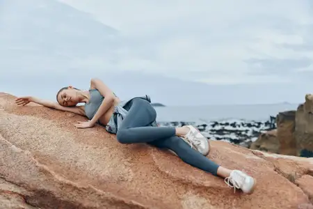 Модная молодая женщина в спортивной одежде лежит на каменистом пляже, излучая спокойствие и безмятежность