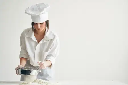 Женщина-пекарь просеивает муку, работая с тестом