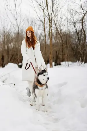 Жизнерадостная женщина в зимней одежде выгуливает собаку в снегу, зимние каникулы