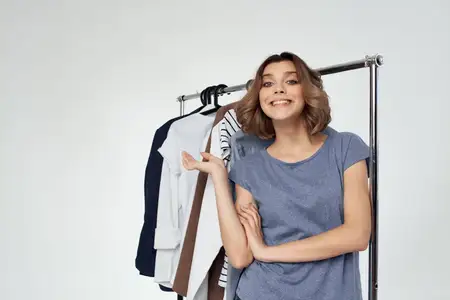 Симпатичная женщина стоит рядом с одеждой, она шопоголик, светлый фон