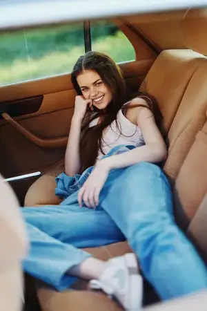 Веселая молодая женщина с длинными волосами отдыхает в автомобиле, наслаждаясь теплым летним днем