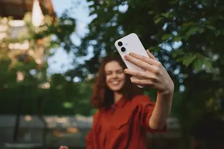 Радостный портрет женщины на улице, улыбающейся, держа смартфон для селфи